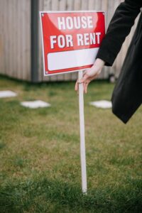 A renter hands keys to a property owner in a suburban backyard with green grass and blooming shrubs.