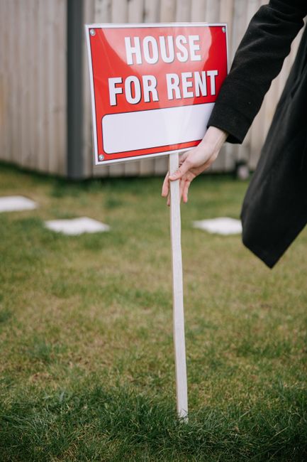 A renter hands keys to a property owner in a suburban backyard with green grass and blooming shrubs.